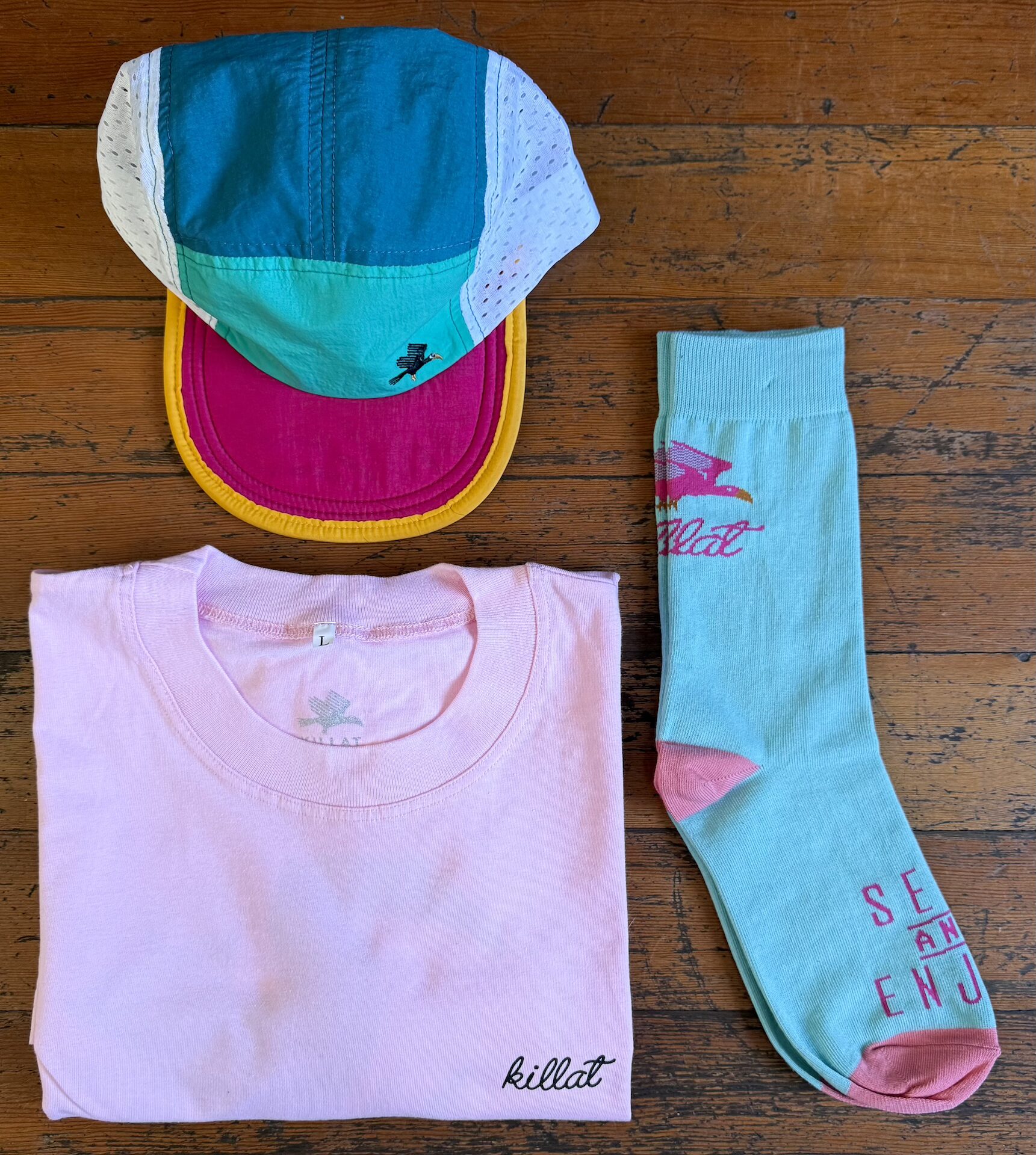 Pink shirt, teal and pink socks and a trail cap in jade gold and teal on a wooden table