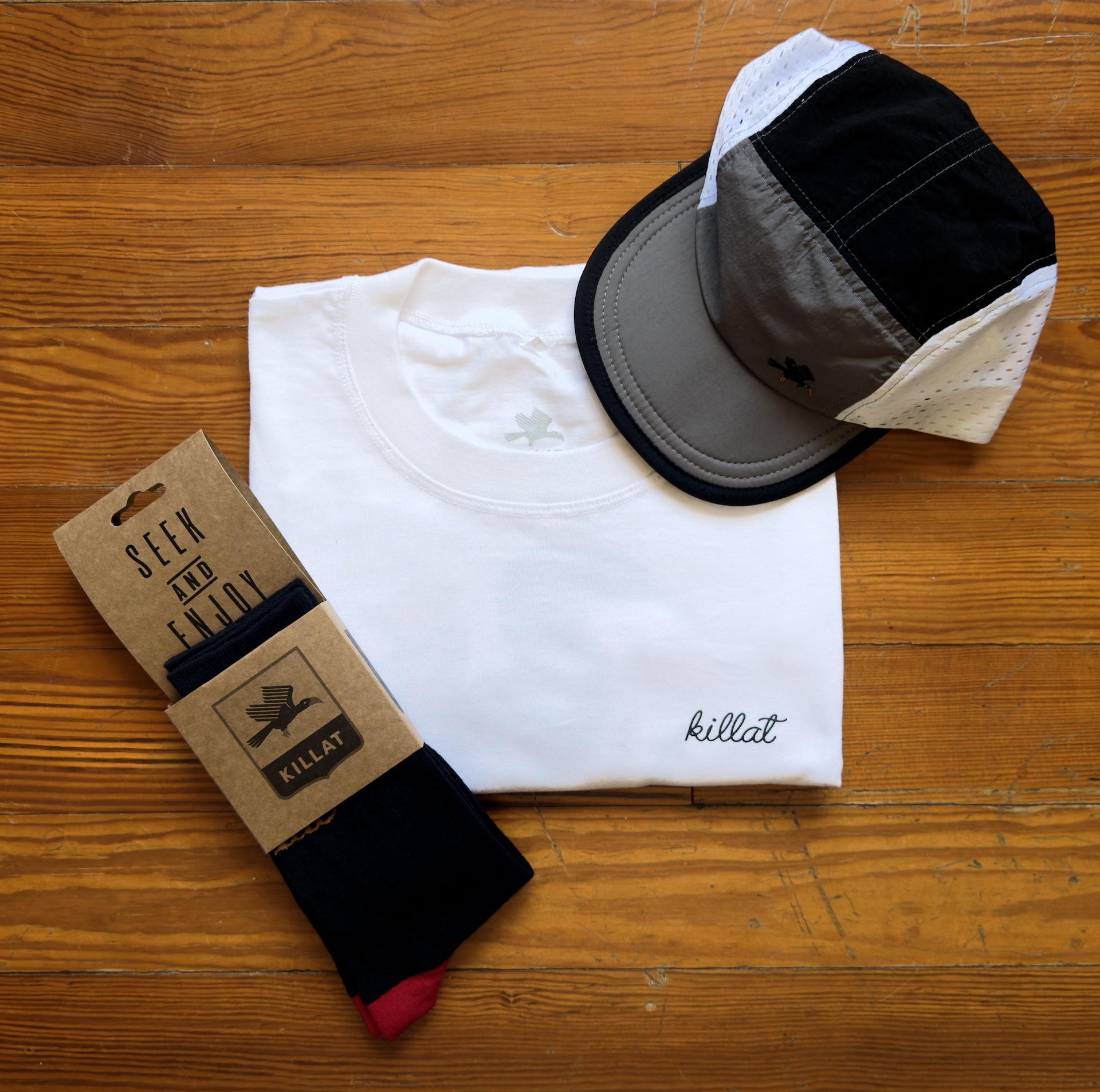 White shirt, black and red socks wrapped and a trail cap in grey and black on a wooden table