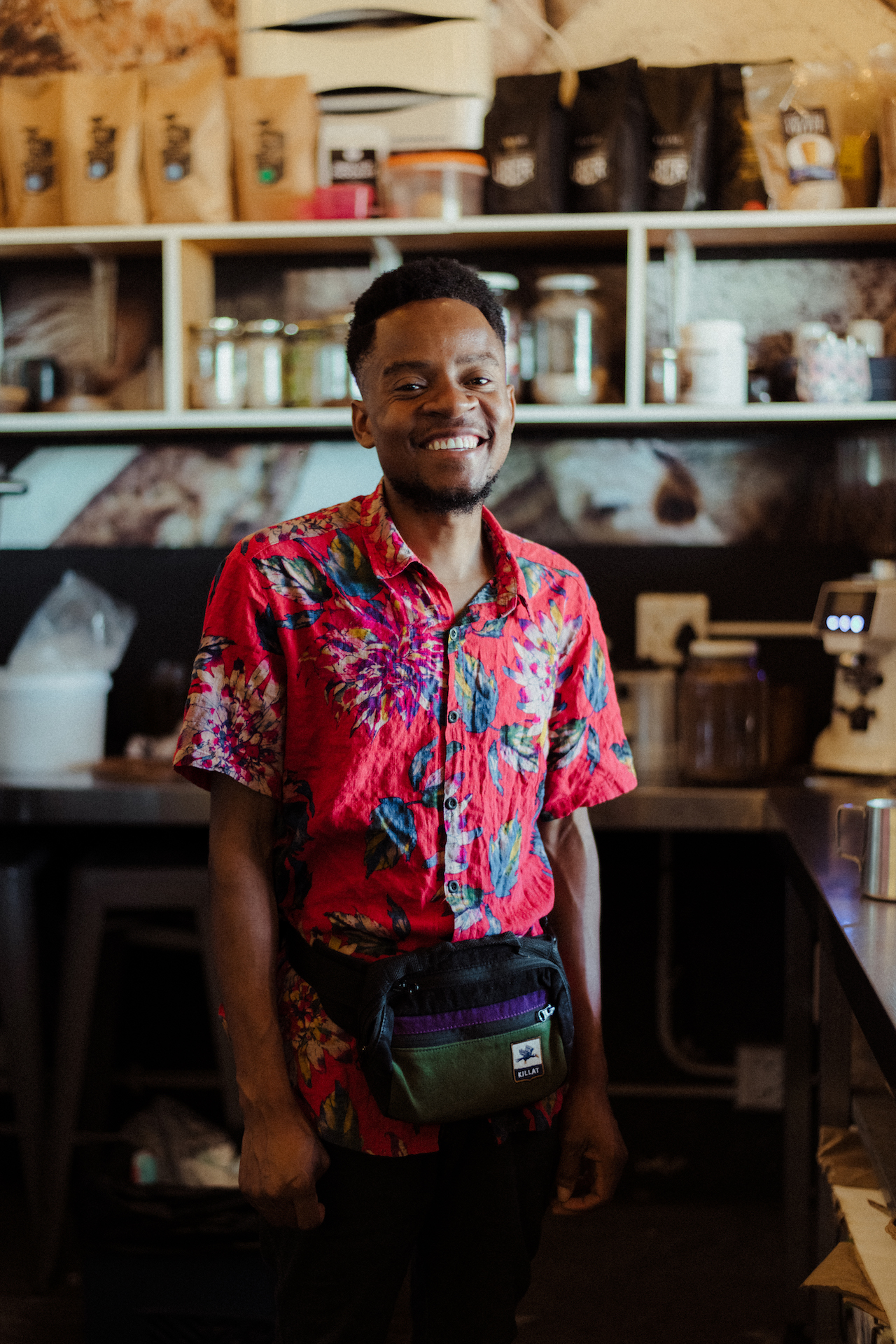 Barista Rodney rocking a hip bag in front of his coffee machines and beans.