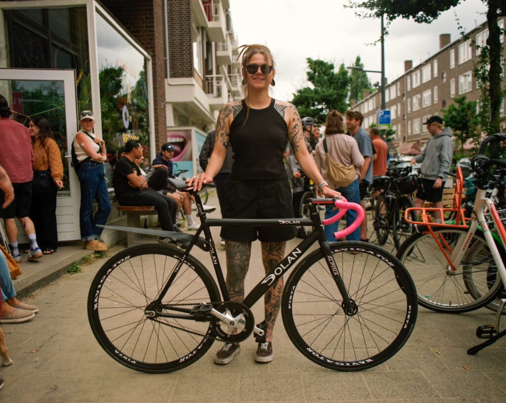Women holding her bike with nice pink handlebar tape in front of a group of people on the streets of Rotterdam at the start of an Alleycat race